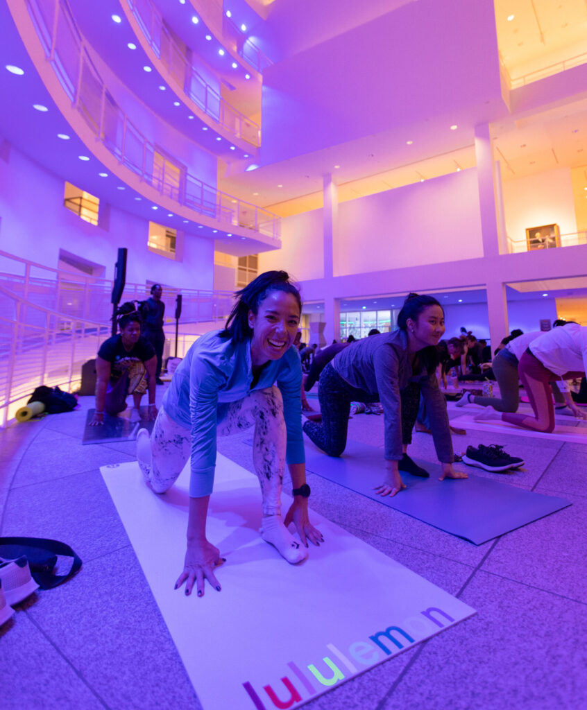 A woman smiles while performing yoga in a large space with purple lights