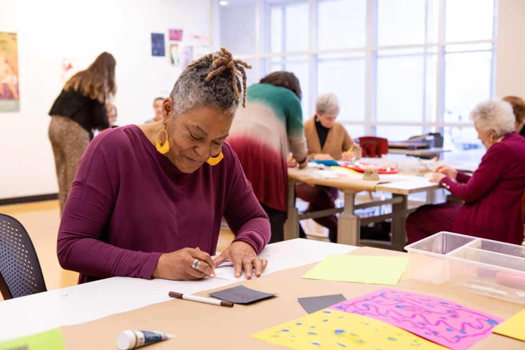 Woman looks down and smiles while working on an art making project