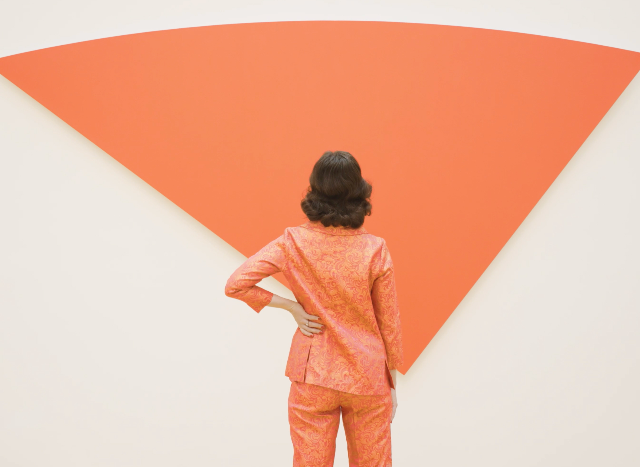Brunette woman in a red pantsuit stands in front of a triangular wedge by Ellsworth Kelly.