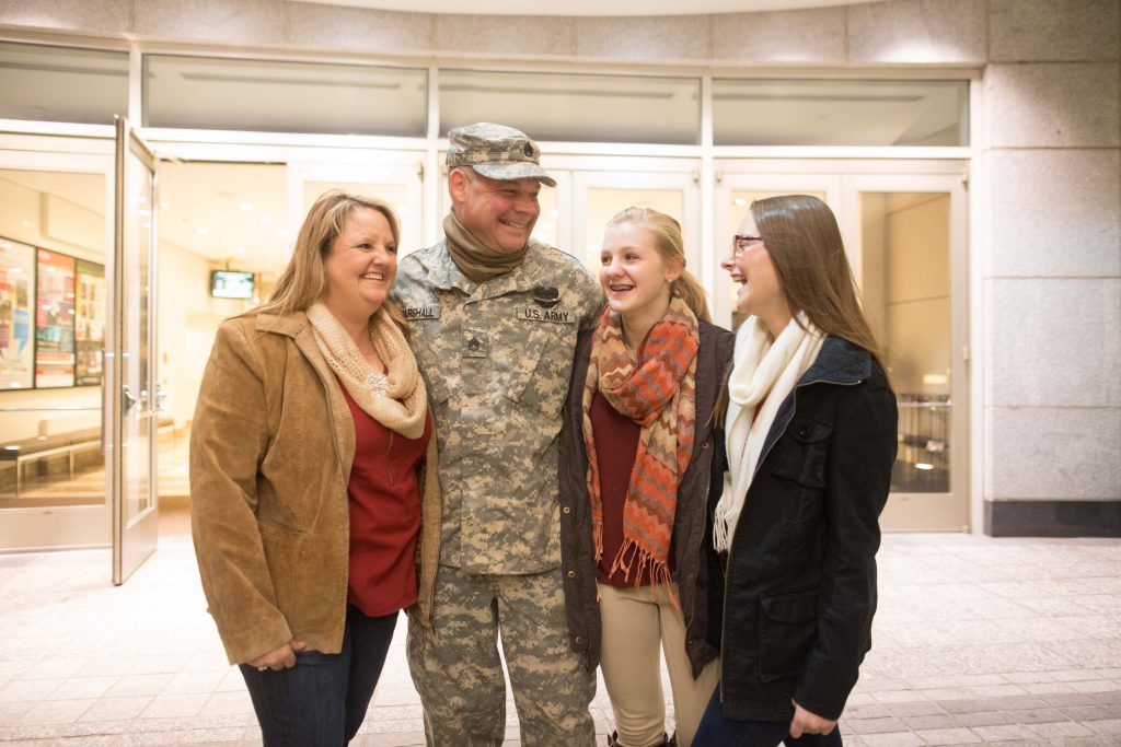 Veterans Discounts Woodruff A military service member smiles in his uniform surrounded by his wife and two daughters.
